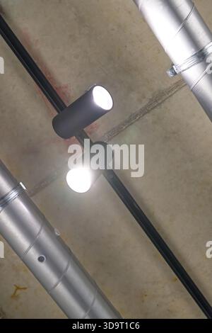 Two modern ceiling lights mounted on a concrete ceiling with exposed metal pipes. Stock Photo