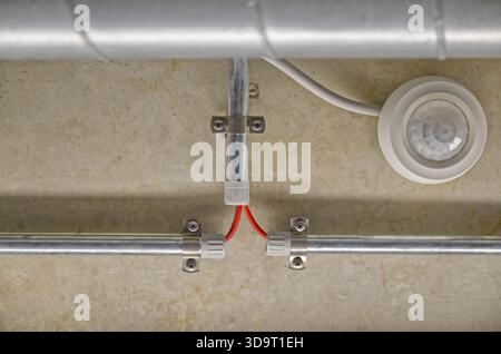 Ceiling-mounted motion sensor with exposed electrical wiring in a conduit. Stock Photo