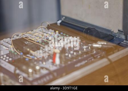 Close-up of an audio mixing console with various knobs and cables, accompanied by a microphone in a case. Stock Photo