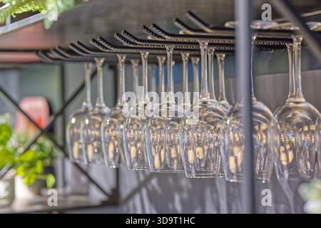 Row of upside-down wine glasses hanging from a rack in a bar setting. Stock Photo