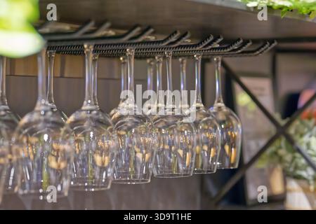 A row of upside-down wine glasses hanging from a rack in a bar setting. Stock Photo