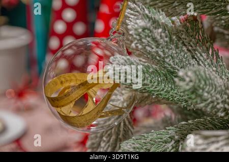 A close-up of a Christmas tree branch with a clear glass ornament containing a curled sheet of music inside. The background is blurred with festive co Stock Photo