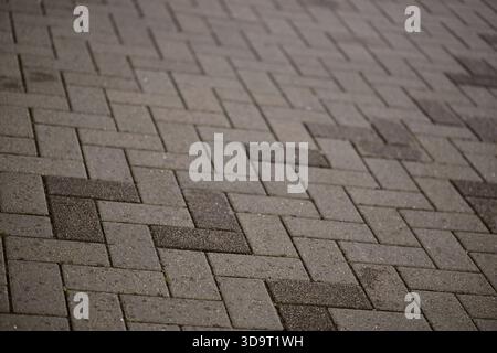 A close-up view of a patterned pavement made of rectangular stones arranged in a herringbone pattern. The surface is textured and features various sha Stock Photo