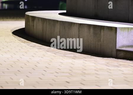 A close-up view of a curved stone bench and pavement at night, illuminated by soft lighting. The texture of the stone and the pattern of the bricks ar Stock Photo