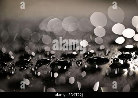 A close-up view of water droplets on a surface, creating a bokeh effect with blurred lights in the background. The image showcases various sizes of dr Stock Photo