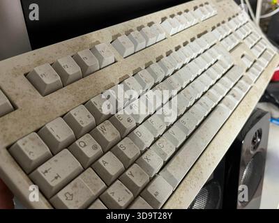 A closeup view of a dusty, old computer keyboard with worn-out keys. The keyboard is positioned at an angle, showing its dirty surface and faded lette Stock Photo