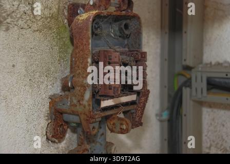 A rusty electrical panel mounted on a wall, showing several switches and a weathered appearance. The background features a textured wall and some elec Stock Photo
