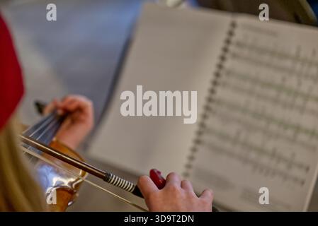 A close-up of a person playing the violin, focusing on their hands and the instrument. Sheet music is visible in the background, indicating a musical Stock Photo