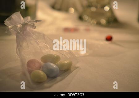 A small transparent bag filled with pastel-colored candy eggs placed on a table with a blurred background. The candies are in shades of pink, blue, an Stock Photo