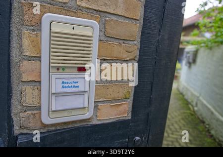 A close-up of a visitor intercom system mounted on a brick wall. The intercom features a speaker, a button, and a label indicating 'Besucher Redaktion Stock Photo