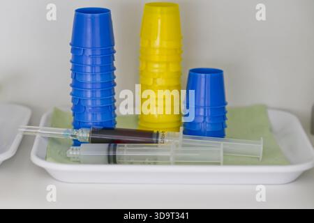 A tray containing medical syringes and colorful plastic cups. The cups are stacked, with blue and yellow colors visible. The syringes are arranged on Stock Photo