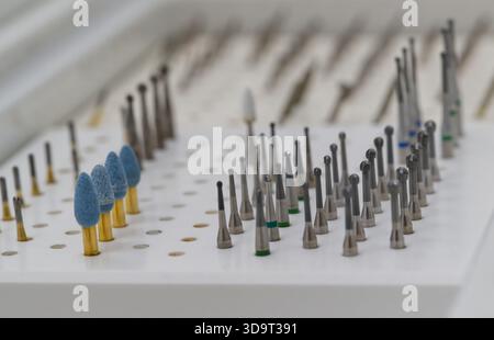 A close-up view of various dental drill bits and tools organized on a white tray. The tools vary in shape and size, with some featuring colored tips. Stock Photo