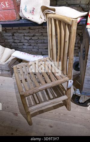 Rustic wooden chair made from natural logs, featuring a slatted seat and backrest. The chair is placed on a wooden floor with a textured wall in the b Stock Photo