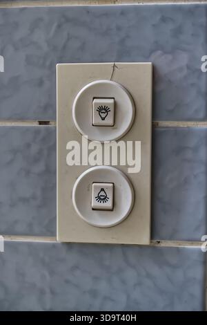 Retro vintage very old dual button panel on a tiled wall, featuring symbols for Light Up and Light below, so you can decide if Light from the ceiling Stock Photo