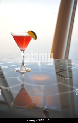 A vibrant cocktail in a martini glass with a slice of lime, reflecting on a glossy surface. The background features soft lighting, creating an elegant Stock Photo