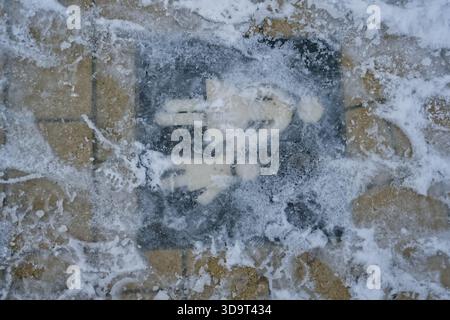 A snow-covered pedestrian crossing sign on a brick pavement, partially obscured by ice and snow. Stock Photo