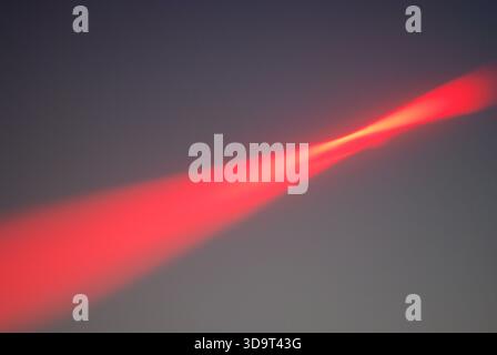 A striking red Laser light beam cutting through a soft gray sky, creating a dramatic visual effect. The light appears to emanate from a point, spreadi Stock Photo
