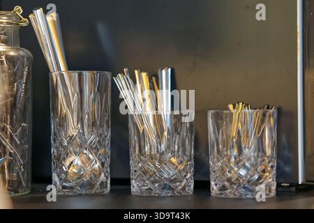 Three crystal glasses holding metal straws on a dark surface. Stock Photo