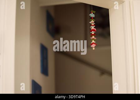 A decorative hanging ornament made of colorful figures, suspended from a doorway. The background features a blurred staircase and blue wall art. Stock Photo