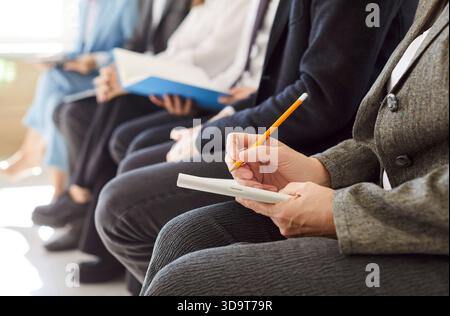 Business people sitting in a row working during a meeting or job conference making notes in notepad Stock Photo