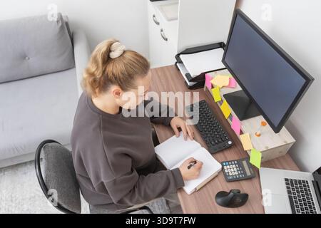 High angle shot of a female professional working from home, writing notes in a planner at her remote desk setup. for themes related to freelancing, fi Stock Photo