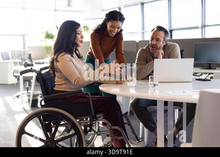 Diverse coworkers collaborating around round table in modern office using tablet and laptop Stock Photo