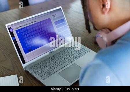 Silver laptop displaying marketing UI resting on wooden desk with pink headphones and notepad Stock Photo