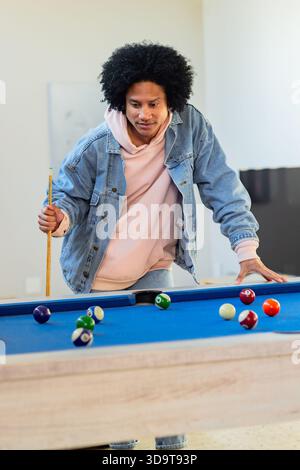 African American man leaning in game room at blue-felt pool table gripping cue among billiard balls Stock Photo