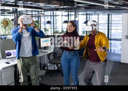 Diverse colleagues collaborating using VR headsets analyzing chart data on office monitors Stock Photo