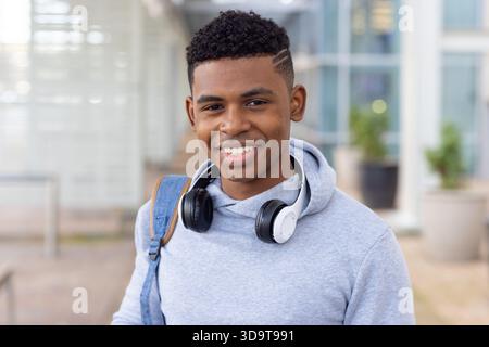 African American adult male smiling while standing at entrance wearing hoodie headphones, backpack Stock Photo