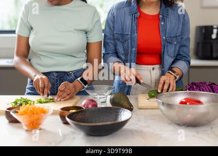 Diverse female friends slicing vegetables on marble countertop in home kitchen with wooden boards Stock Photo
