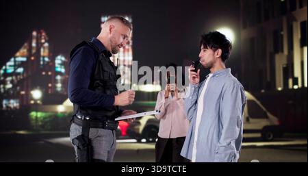 Police Officer Conducts Breathalyzer Test During Traffic Stop; Bystander Films. Stock Photo