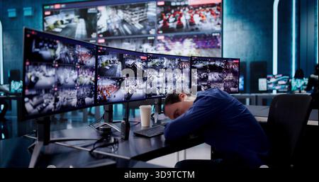 Sleeping Security Guard Monitoring Multiple CCTV Cameras At His Desk. Stock Photo