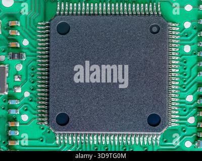 Extreme close-up of a green printed circuit board (PCB) dominated by a large square black integrated circuit. Stock Photo
