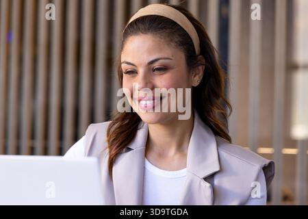 Woman in her 30s wearing beige blazer over white top working on laptop in coworking space Stock Photo