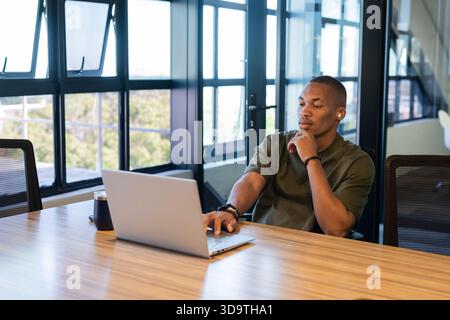 African American man sitting at wooden table in modern office typing on silver laptop, copy space Stock Photo