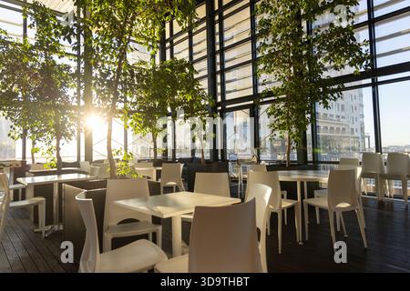 White tables and chairs are basking in low-angle sunlight at high-rise cafe, casting long shadows Stock Photo