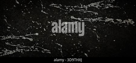 Gritty, dark asphalt texture splattered with streaks and droplets of rough, pale gray or white paint, creating an abstract, grungy, and urban backgrou Stock Photo