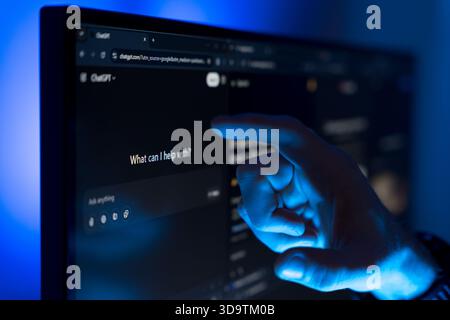 Hand pointing at ChatGPT interface on computer screen with blue light Stock Photo
