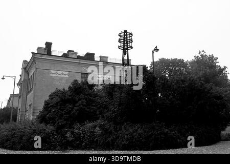 Black and white view of a plaster building and metal lattice tower above leafy shrubs on a misty morning at Suomenlinna Island, Helsinki, Finland. Stock Photo
