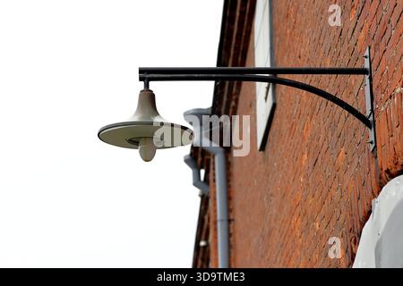 Wall mounted metal street lamp with curved bracket on a red brick facade, close up on a soft misty morning at Suomenlinna Island, Helsinki, Finland. Stock Photo