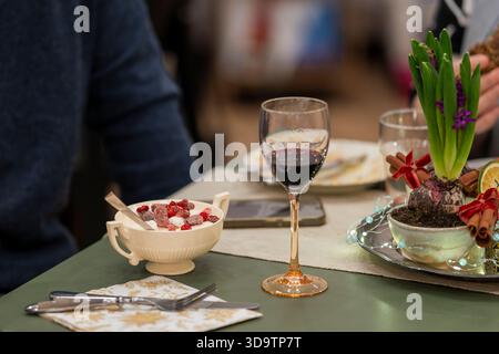 Festive table setting with winter dessert, red wine, and holiday decorations. Cozy holiday dining scene with berries, mulled wine vibes. Stock Photo