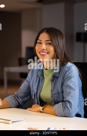 Asian Indian woman typing on keyboard while viewing pie and bar charts at modern office desk Stock Photo