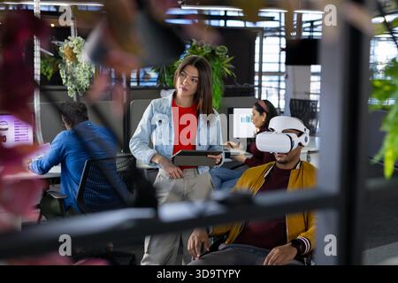 Diverse coworkers presenting virtual reality project in open-plan office using tablet and computers Stock Photo