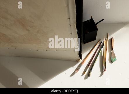 Backside of stretched canvas lying on white table with fanned brushes, palette knife, brush holder Stock Photo