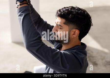 Indian man raising arms overhead stretching on terrace with beaded bracelet and smartwatch Stock Photo