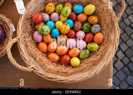 Brightly colored ceramic Easter eggs with speckled patterns lie together in a straw-filled basket, creating a cheerful spring and holiday decoration. Stock Photo