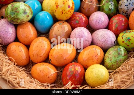 Brightly colored ceramic Easter eggs with speckled patterns lie together in a straw-filled basket, creating a cheerful spring and holiday decoration. Stock Photo