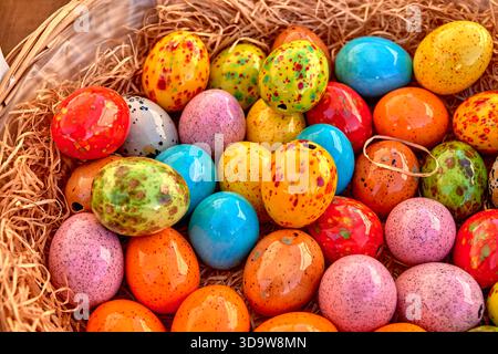 Brightly colored ceramic Easter eggs with speckled patterns lie together in a straw-filled basket, creating a cheerful spring and holiday decoration. Stock Photo
