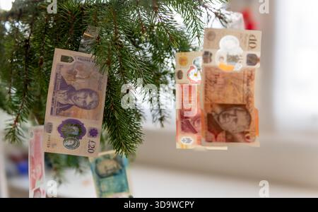 A UK Christmas expenses concept with a closeup of various Pound Sterling bank notes hanging on a Christmas tree as decorations. Stock Photo